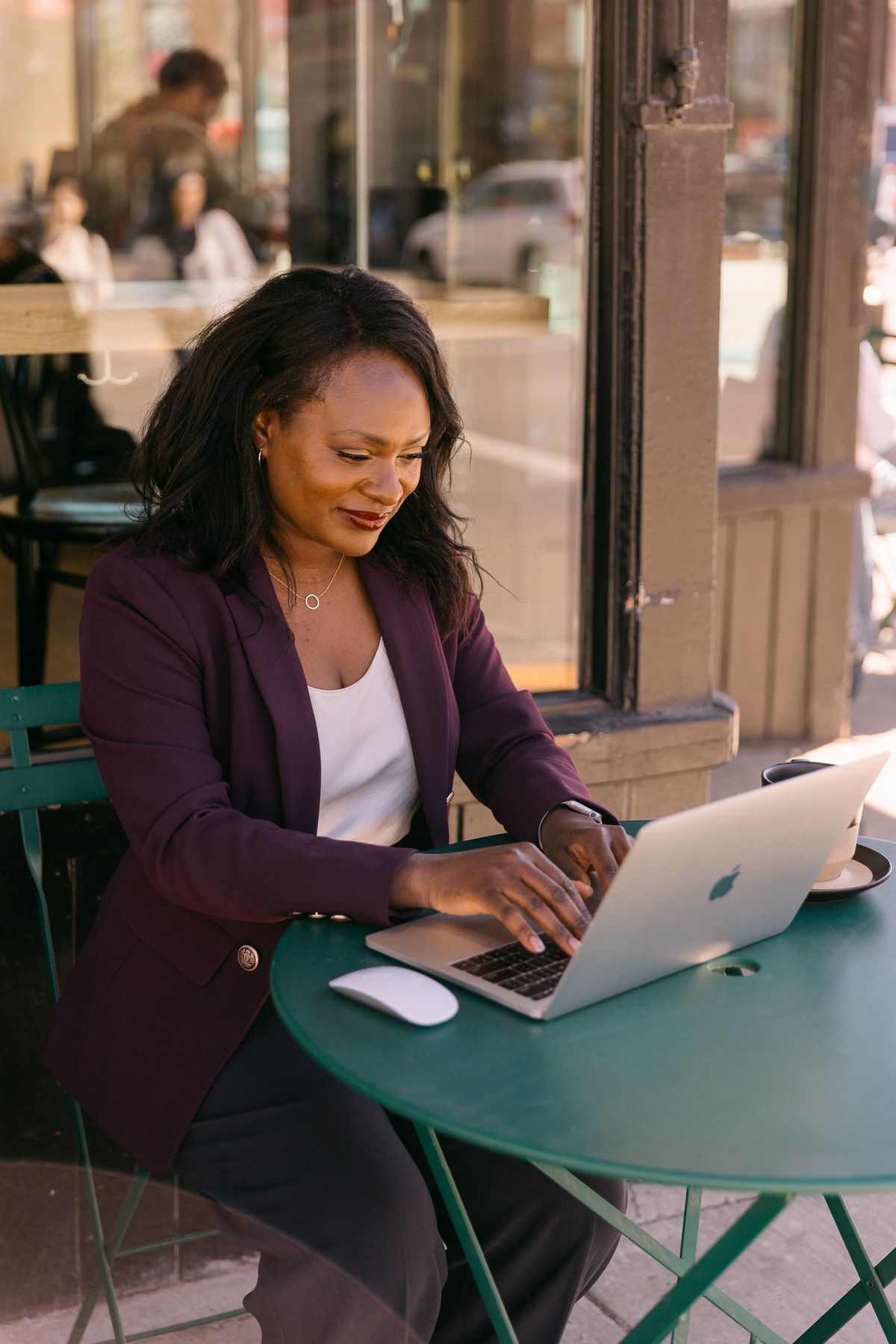 Rozella smiling as she works on her laptop at an outdoor cafe table